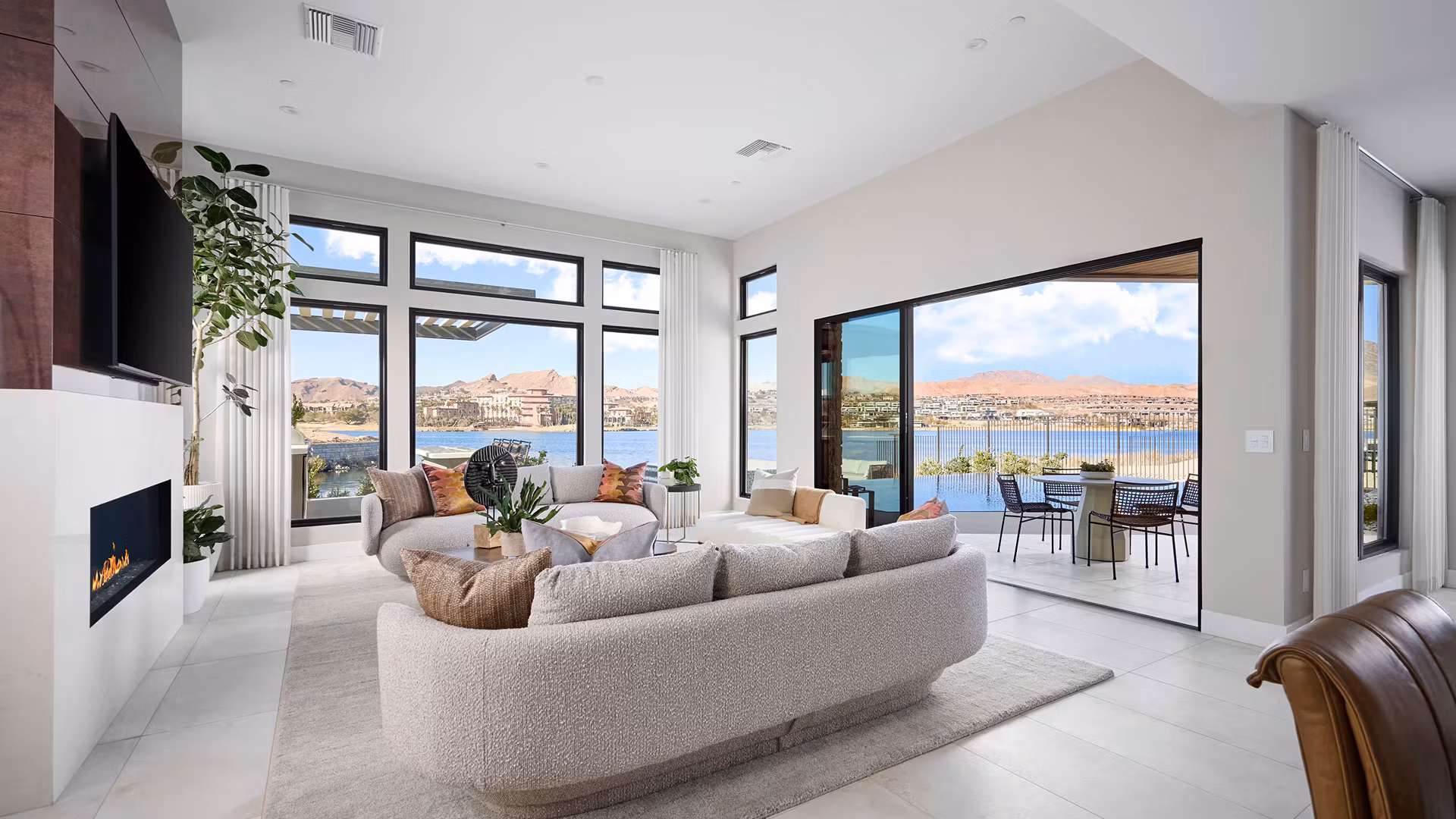 A spacious and modern living room with large windows overlooking a scenic lake and mountains in the background.