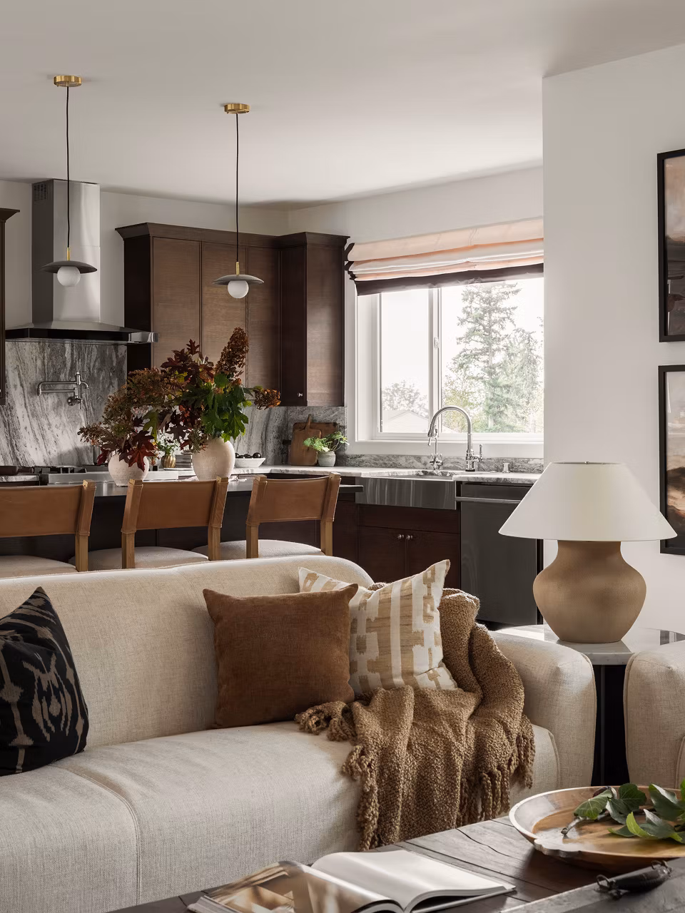 A cozy and inviting living room with a plush beige sofa, complemented by a modern kitchen with dark wood cabinetry and a large window overlooking a scenic outdoor view.